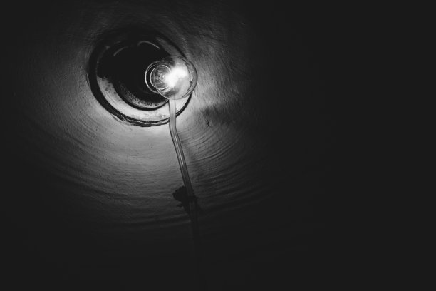 白炽灯在暗室里燃烧特写。照明。粗糙墙上的旧灯泡。地下室的灯光呈灰度。光在黑暗中。极简主义的单色背景。副本的空间。图片下载