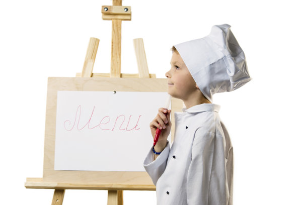 穿着厨师服的可爱男孩在纸上准备菜单图片下载