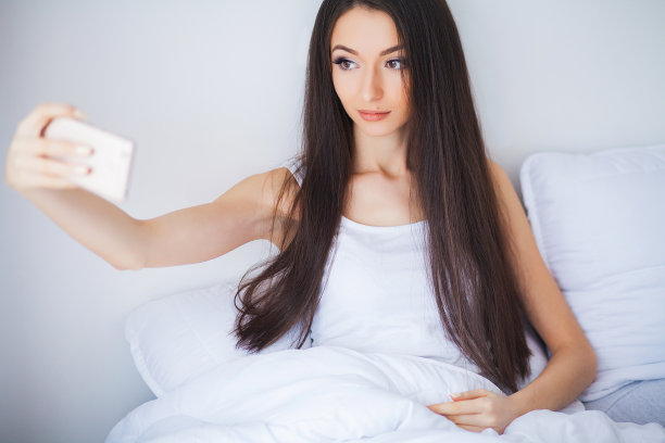 快乐可爱的女人躺在床上用手机图片下载