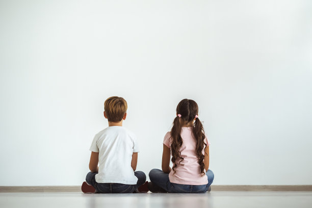 一个女孩和一个男孩坐在白色墙壁背景的地板上图片下载