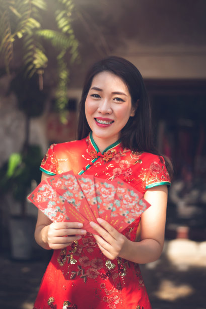 美丽的亚洲女子身穿红色旗袍，手持红包，喜迎中国新年素材图片