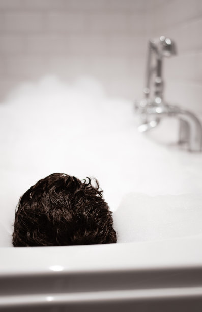 一个男人的后脑勺，他的头发卷曲卷曲，他躺在一个满是泡沫的浴缸里图片下载