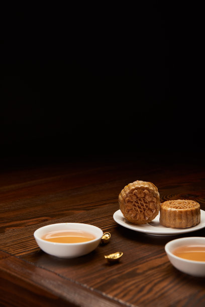 黑色背景下的传统月饼、茶杯和金元宝素材图片