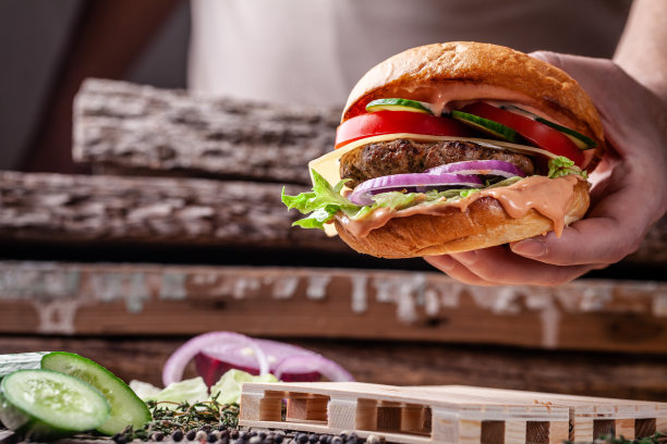 美式烹饪的概念。一个男人自制的汉堡，里面有小圆面包、牛肉和猪肉片、西红柿、黄瓜、红洋葱，还有番茄酱和蛋黄酱。汉堡在小托盘上图片下载
