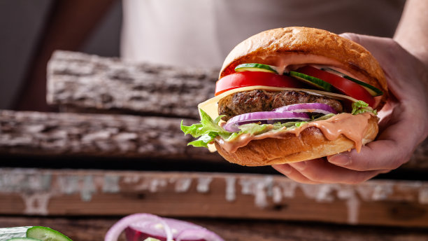 美式烹饪的概念。一个男人自制的汉堡，里面有小圆面包、牛肉和猪肉片、西红柿、黄瓜、红洋葱，还有番茄酱和蛋黄酱。汉堡在小托盘上图片下载