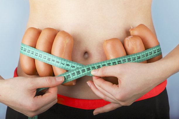 一位年轻女子用香肠量她的细腰。图片下载