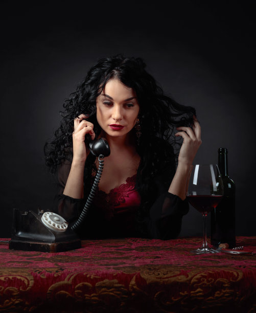 一个迷人的黑发女人的肖像和旧电话和红酒。图片下载
