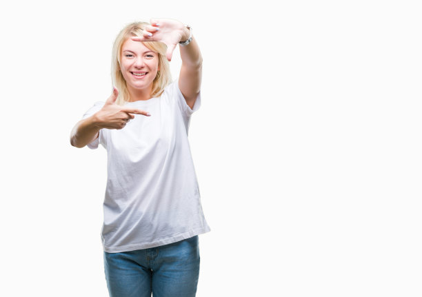 年轻美丽的金发女人穿着白色t恤在孤立的背景微笑，使框架与手和手指与幸福的脸。创意和摄影概念。图片下载