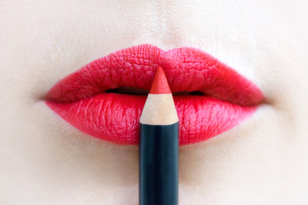 特写的美丽女性的嘴唇，画在明亮的红色。唇线笔接触到双唇图片下载