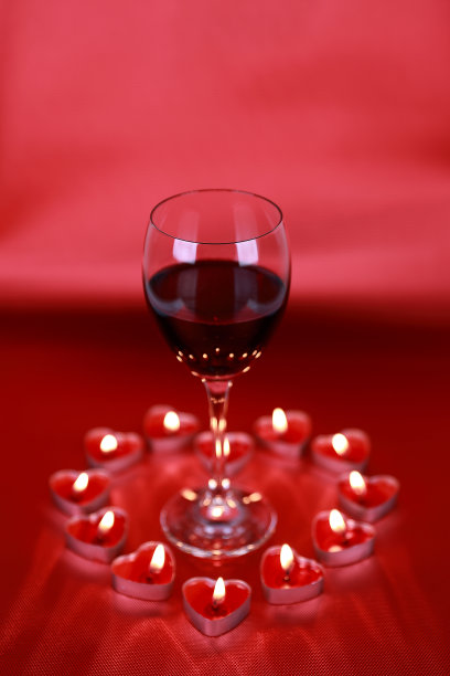情人节，一杯红酒配上红色背景的心形蜡烛。图片下载
