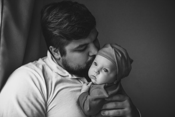 一位年轻的父亲亲吻他刚出生的女儿。父亲和新生儿特写。图片下载