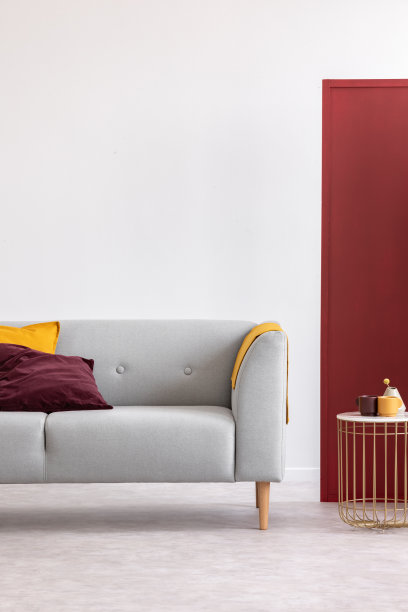 在白色和红色的客厅里，金色的桌子紧挨着灰色的长椅，枕头和毯子。真实的照片图片下载