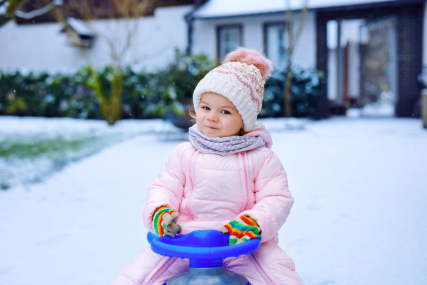 可爱的蹒跚学步的小女孩在雪地上享受雪橇之旅。孩子玩雪橇。小孩子穿着五颜六色的时尚衣服坐着雪橇。户外活动的乐趣，为家庭的寒假一天下雪图片下载