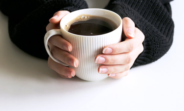 特写的女人的手在黑色针织毛衣拿着一杯咖啡。空白的马克杯模型场景。冬天的设计。女性风格的库存照片。图片下载