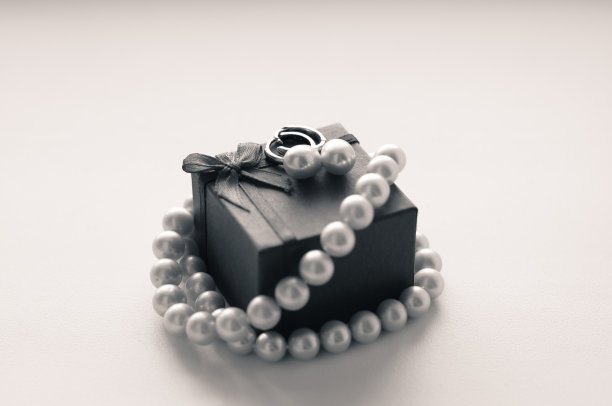 一对耳环和一串珍珠放在一个以白色为背景的首饰盒上。黑白照片。图片下载