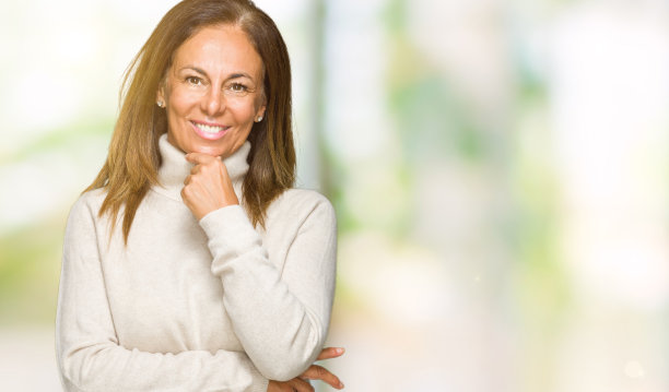 美丽的中年成年女性穿着冬季毛衣在孤立的背景看起来自信地看着镜头，双臂交叉，手举在下巴上。积极的思考。图片下载