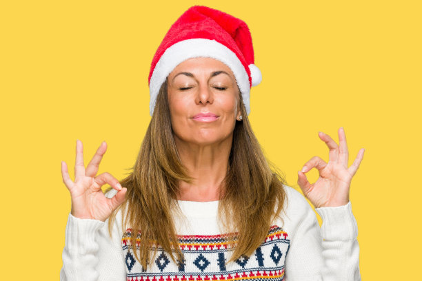 中年成年妇女穿着冬季毛衣和圣诞帽在孤立的背景放松和微笑，闭上眼睛做冥想手势与手指。瑜伽的概念。图片下载