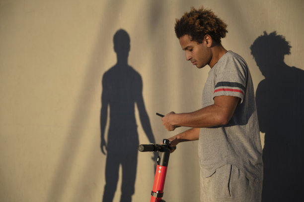 在美国加州威尼斯海滩，这位年轻的拉丁裔男子用他的智能手机预订了电动滑板车图片下载