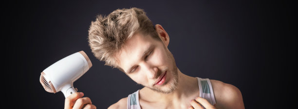 年轻男子用电吹风吹他的头发图片下载