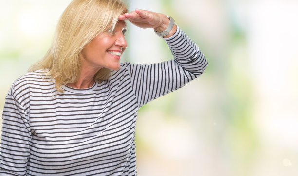 中年金发女人在孤立的背景非常快乐，微笑着看远与手在头上。搜索概念。图片下载