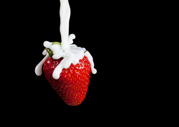 草莓溅起水花。孤立在黑色背景上。微距照片的草莓在牛奶溅和滴。图片下载