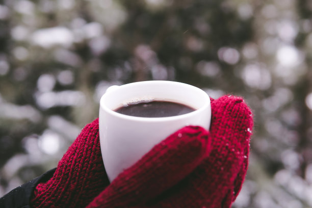 在冬季森林的背景上，一个女孩拿着一个戴着红色手套的咖啡杯图片下载