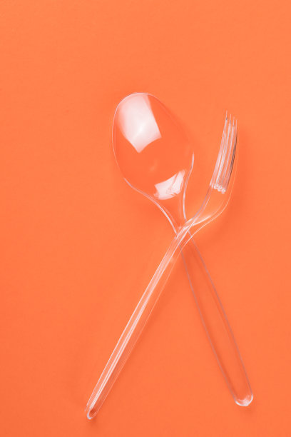 橙色背景上的透明塑料叉子和勺子图片下载