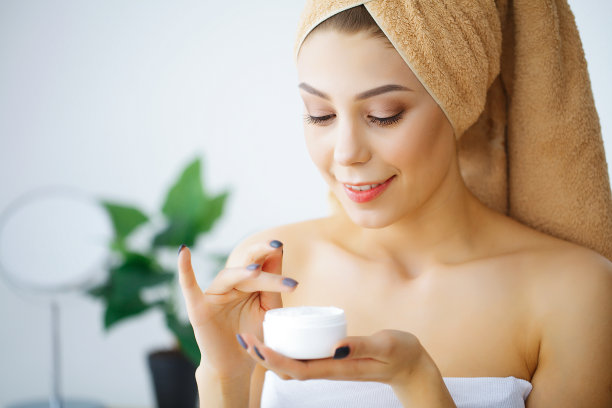 美容和护理。一个头上戴着棕色毛巾的女孩的肖像。年轻女子的纯净肌肤。手里拿着奶油。敷面霜。高分辨率图片下载