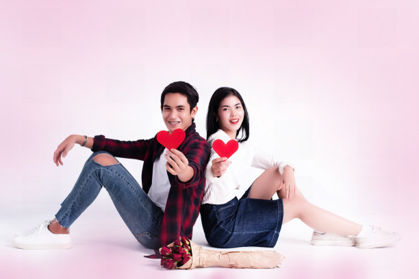 美女和她的男友，浪漫的情侣背靠背坐着，手里拿着红心剪纸，幸福的感觉，甜蜜的情感图片下载