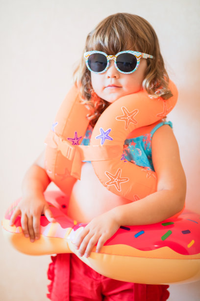 可爱的小女孩准备去海滩，戴着太阳镜，充气套袖浮筒和充气甜甜圈浮筒图片下载