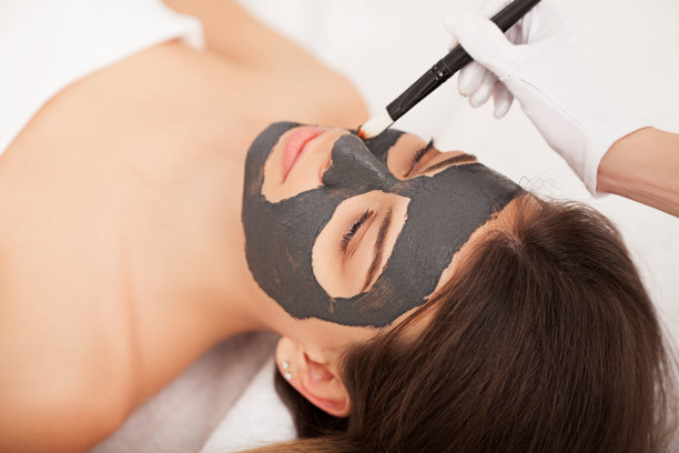 水疗中心。硬件美容。可爱的年轻女人的特写照片与奶油面膜在美容院。图片下载