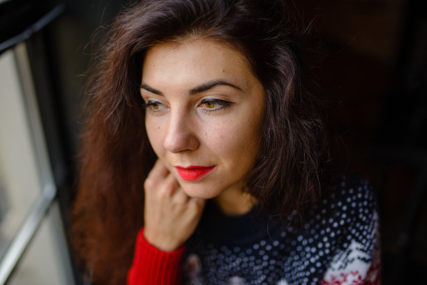 户外肖像迷人的黑发女士摆出浪漫的微笑在雪景。在冬天的街道上，穿着针织帽子和柔软毛衣的漂亮笑女孩的照片。图片下载