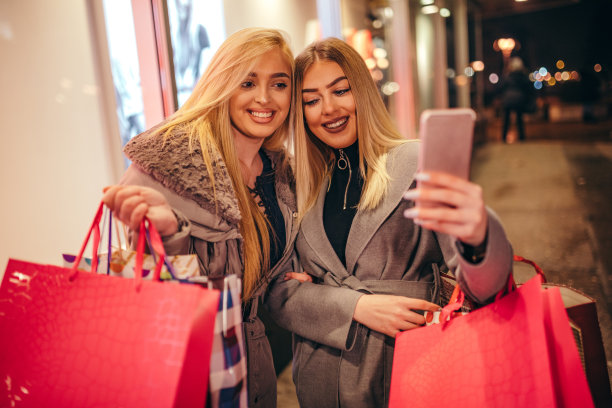 快乐的年轻女性拿着购物袋走在城市里。图片下载