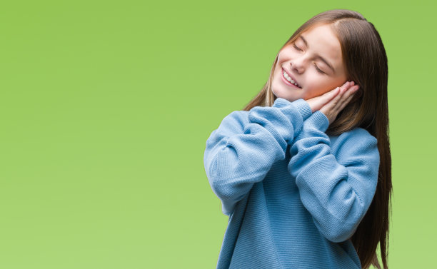 年轻美丽的女孩穿着冬天的毛衣在孤立的背景睡累了，做梦，摆姿势与手在一起，而闭上眼睛微笑。图片下载