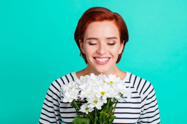 近距离的肖像欢快迷人的狐狸，她的夫人闭上眼睛闻到甘菊在手中高兴的母亲节穿着白色条纹毛衣孤立在蓝绿色的背景图片下载