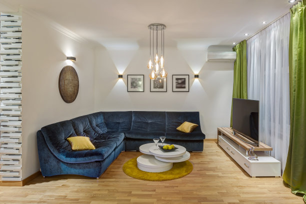 现代的客厅，大的深蓝色沙发与黄色的枕头，玻璃桌子在房间的中心。墙上的创意图片。有电视的舒适地方。内部为绿色，白色和深蓝色。图片下载