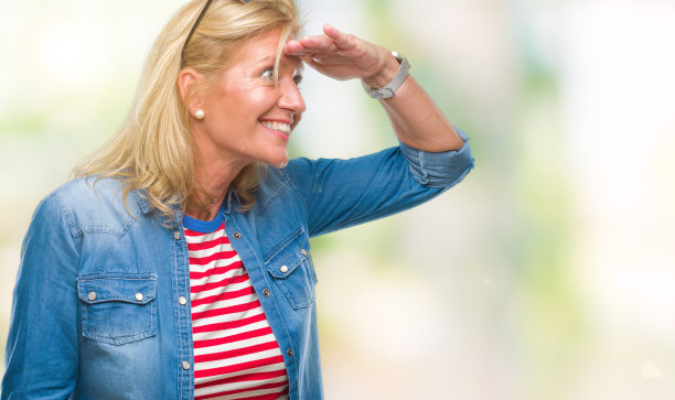 中年金发女人在孤立的背景非常快乐，微笑着看远与手在头上。搜索概念。图片下载