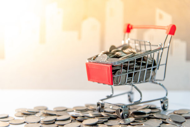 存钱的概念。硬币在迷你购物车中，洒在桌子上，以城市为背景。图片下载