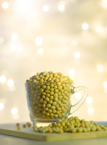 杯中的大豆和大豆堆在抽象的金色闪烁的灯光背景图片下载