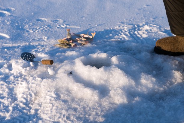 在白雪覆盖的湖面上，鲈鱼和舀冰用的勺子都在洞口附近，可以用来捕鱼。图片下载