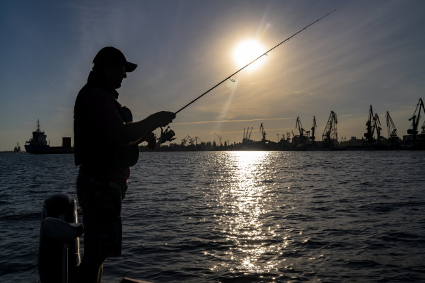 都市渔业的概念。渔民的剪影在工业海港城市的背景。图片下载
