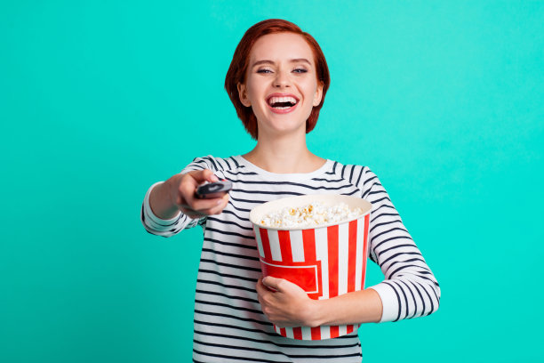 改变通道的概念。近距离的照片肖像，有趣的funky迷人的笑声，漂亮可爱的她，她的夫人抱着盒子与爆米花看着相机孤立明亮的蓝绿色背景图片下载