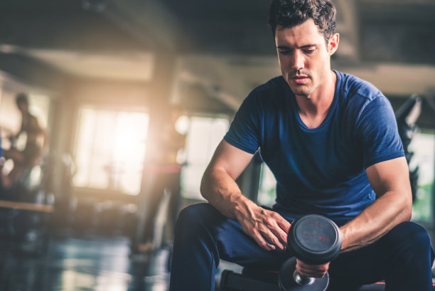 年轻有魅力的健身男子在健身房用机器和哑铃锻炼的电影基调。个人运动，健身身体的肌肉，健康的生活理念图片下载