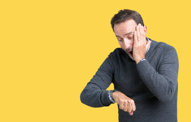 英俊的中年老人穿着毛衣越过孤立的背景看着手表着急的时间，害怕迟到图片下载