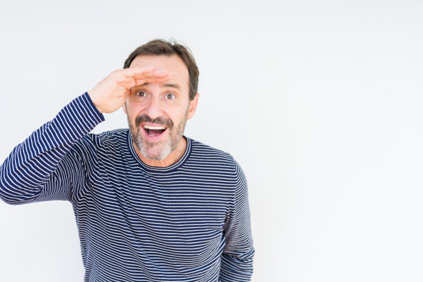 英俊的老男人在孤立的背景下很开心，微笑着望着远方的手在头上。搜索概念。图片下载