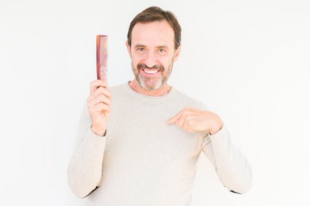 高级男子拿着头发梳在孤立的背景与惊讶的脸指向自己的手指图片下载