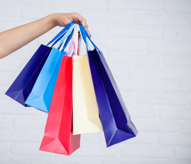 购物。女人拿着彩色纸购物袋的特写在白色的墙壁背景图片下载