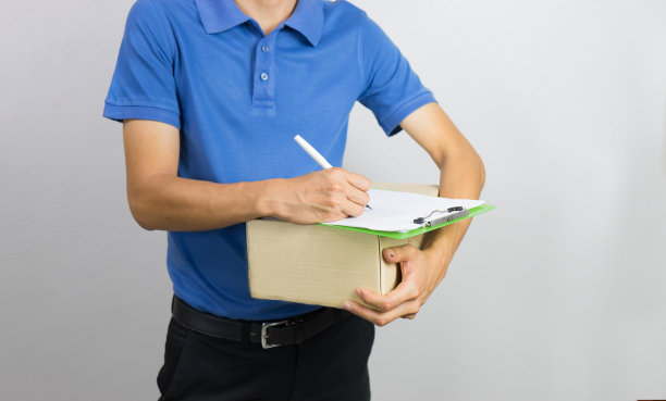 一个年轻的送货员拿着一个纸板箱，把签名放在写字板上图片下载