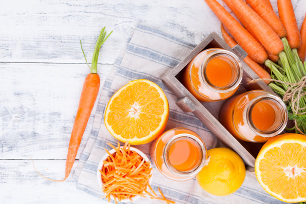 新鲜的胡萝卜汁，橙汁和柠檬汁。胡萝卜与树叶和其他新鲜水果在木背景。罐装饮料，俯视图。图片下载
