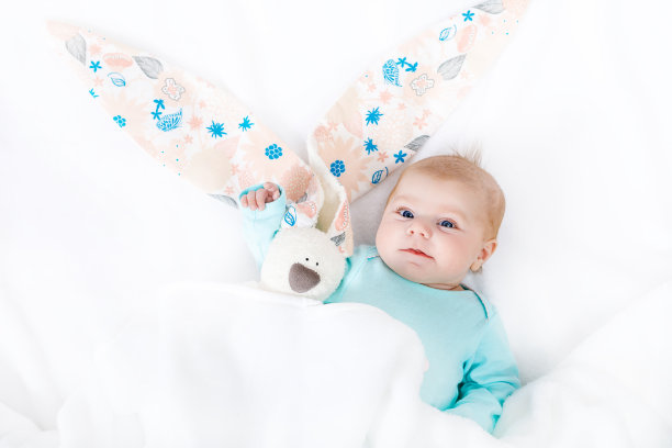 两个月大的新生女婴的特写，白色的背景。可爱的孩子玩着毛绒兔子玩具，耳朵有点长。节日，复活节，童年概念图片下载